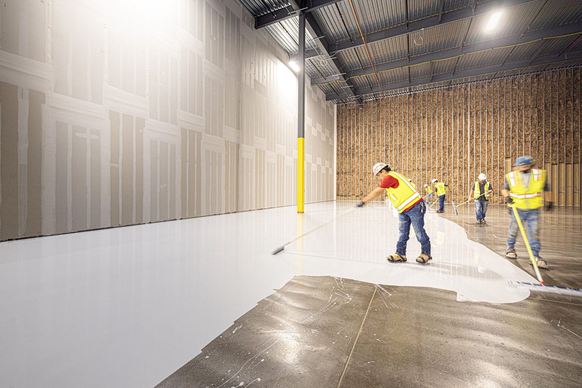 Work crew applying a floor coating with squeegees inside a building